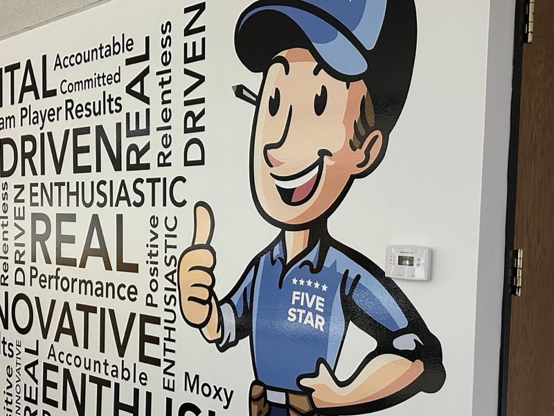 A wall mural of a cartoon mascot in a Five Star shirt giving a thumbs up beside a wall of words