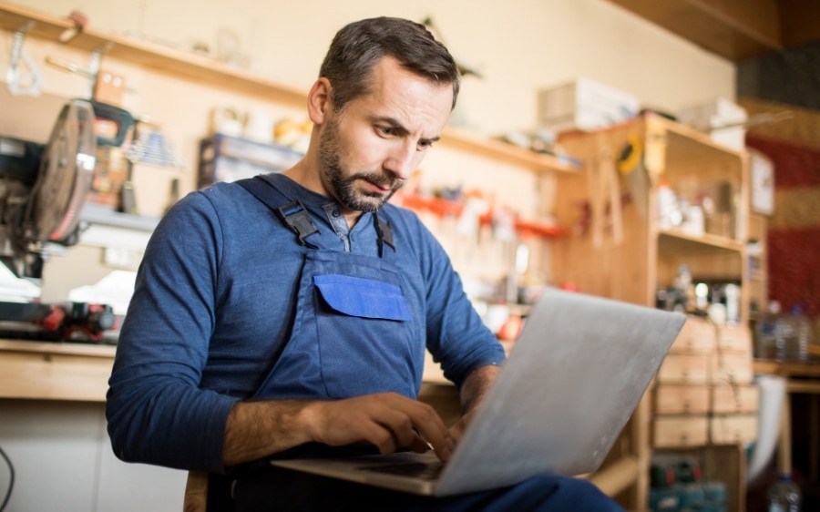 A tradesman at his workbench, working on a laptop between jobs