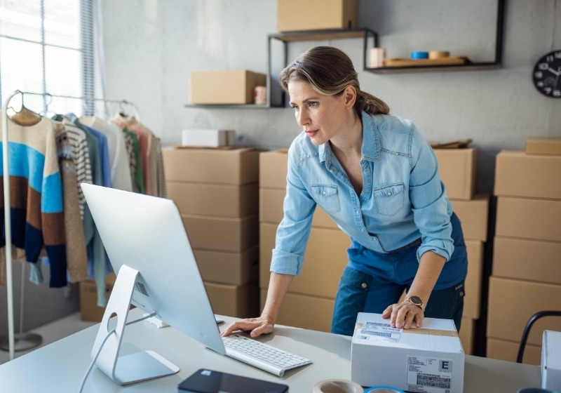 A business owner at her computer in a stockroom full of labelled boxes