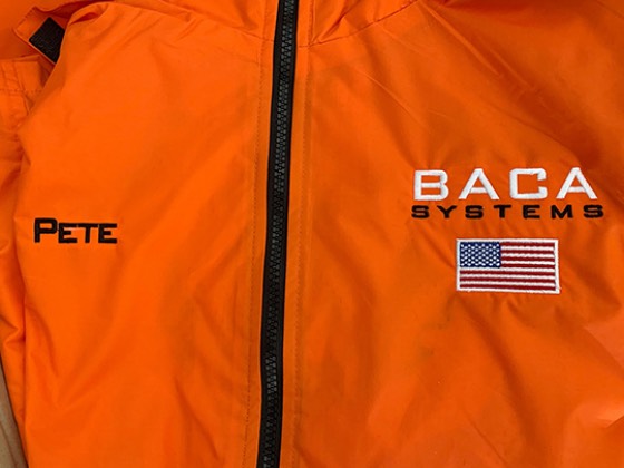 Orange BACA Systems windbreaker with an embroidered logo, an American flag and an employee name
