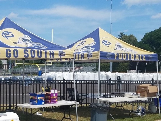 Blue and gold Go South football canopy tents set up beside a stadium