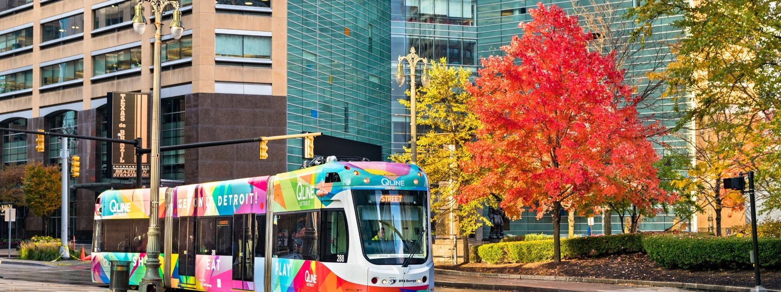 The QLine streetcar passing fall trees on Woodward Avenue in Detroit