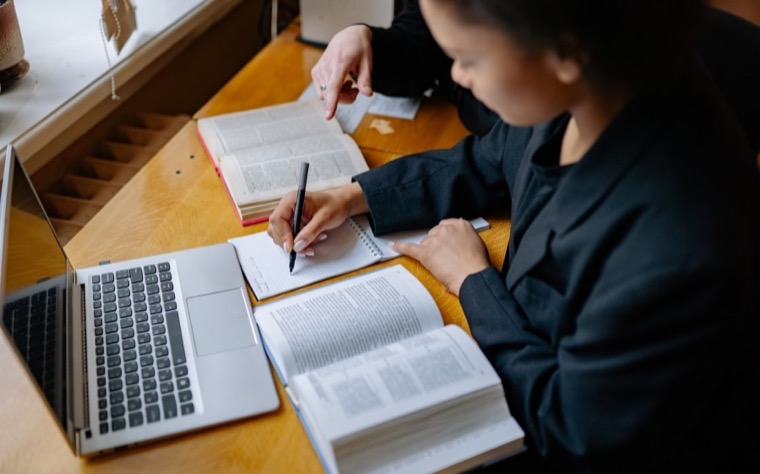 A person cross-referencing an open book beside a laptop