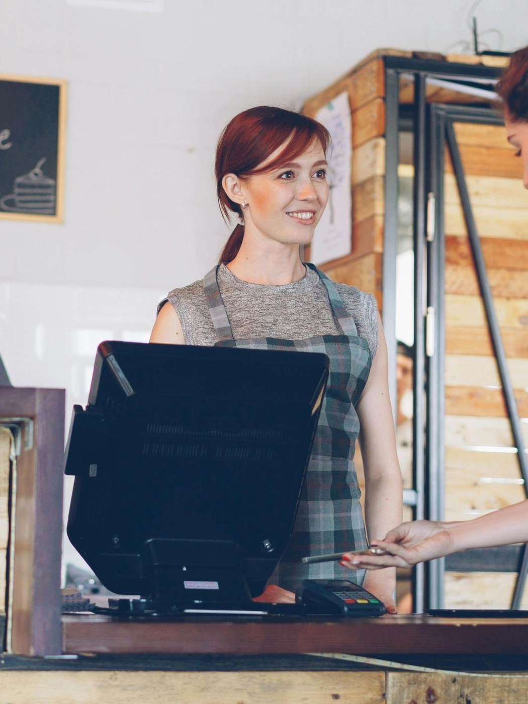 A shop owner holding up a chalkboard sign at her counter